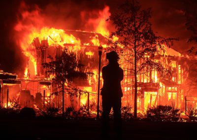 Firefighter gazing upon a crumbling building engulfed in flames